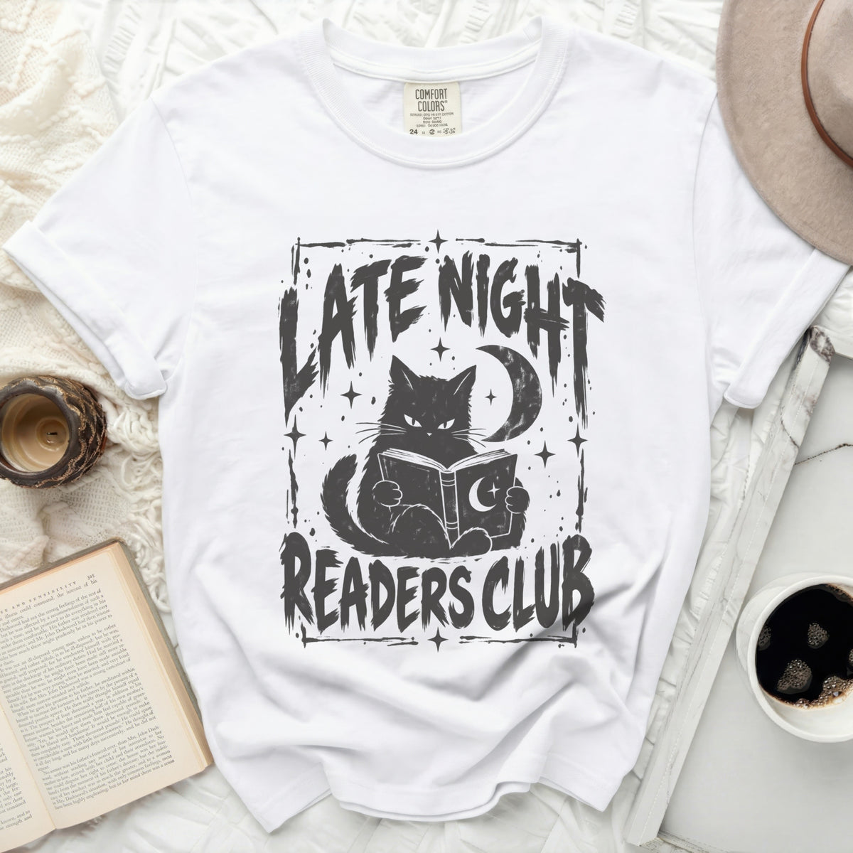 White t-shirt with black graphic of a cat reading a book under a crescent moon, text "LATE NIGHT READERS CLUB".
