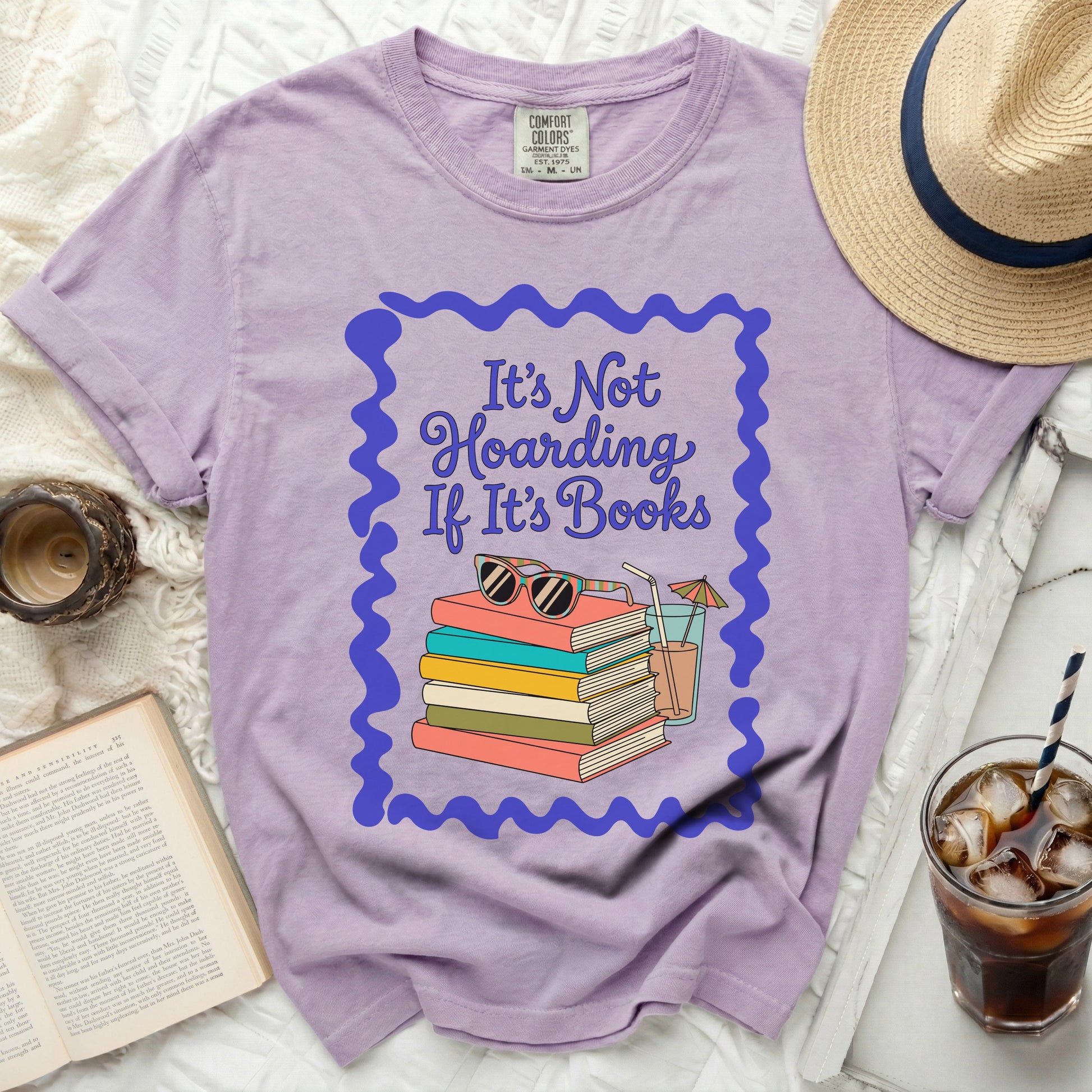 Lavender t-shirt with a graphic of books, sunglasses, and a drink.