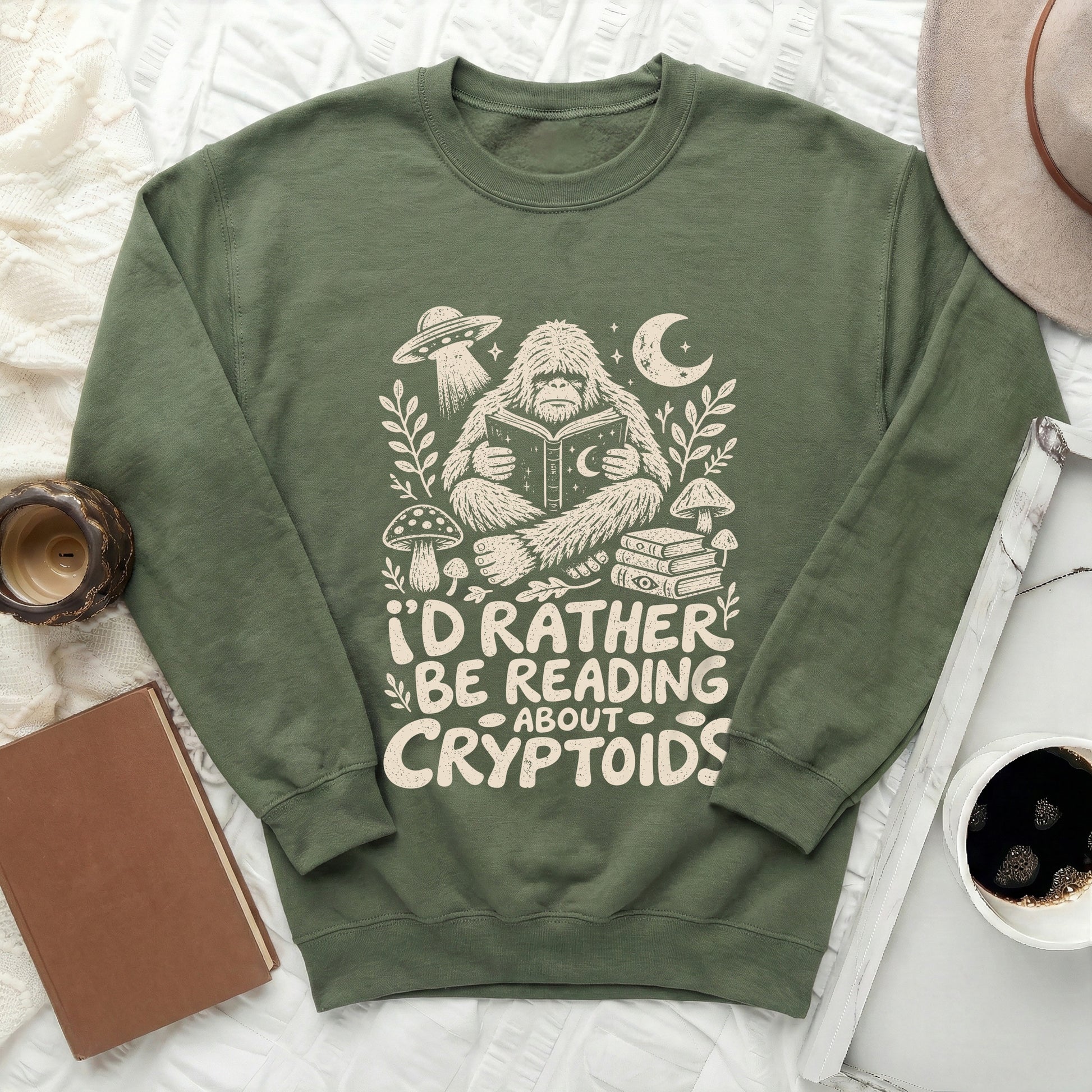 Green sweatshirt with Bigfoot reading a book and text "I'd rather be reading about cryptoids."