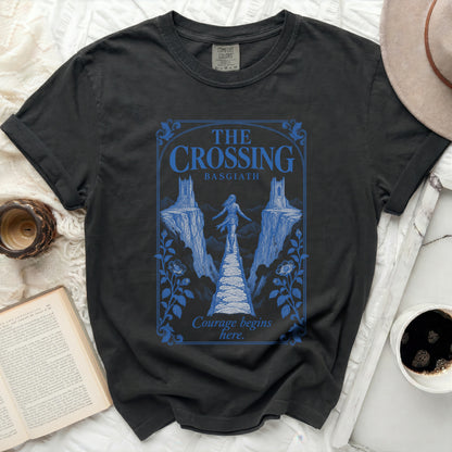 Black t-shirt featuring a blue graphic of a person walking a narrow bridge between two cliffs, with text reading "The Crossing Basgiath" and "Courage begins here."