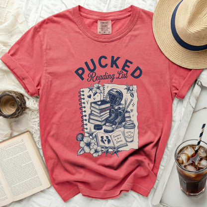 Red t-shirt with "Pucked Reading List" design featuring books, hockey gear, and flowers.