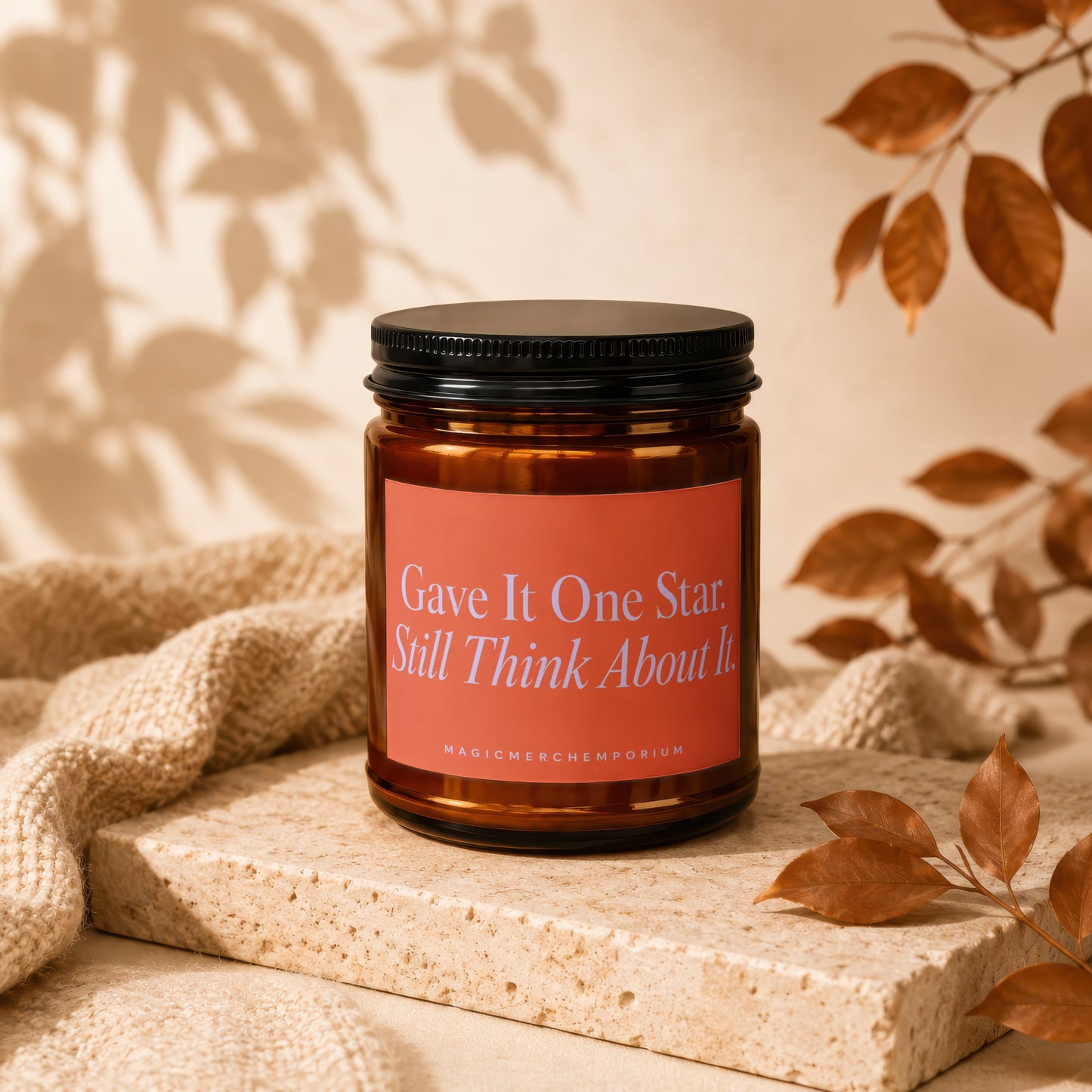 Amber candle with black lid and coral label reading "Gave It One Star. Still Think About It."