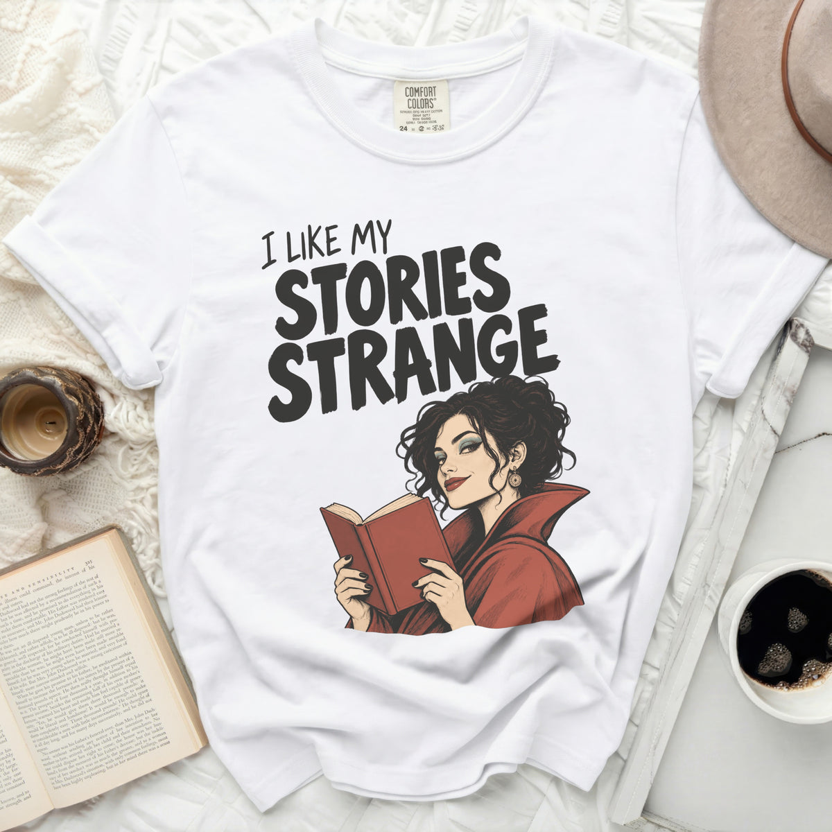 White t-shirt with text "I LIKE MY STORIES STRANGE" and illustration of a woman reading.