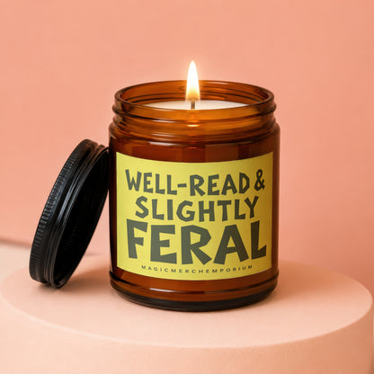 Amber jar candle with lit wick and lid off, reads "Well-Read & Slightly Feral".