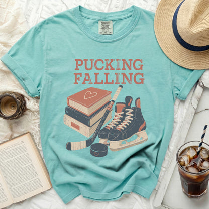 Teal t-shirt with "Pucking Falling" text and hockey gear illustration.