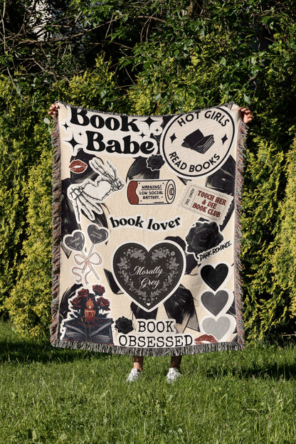 A person is holding up a blanket with various book-related designs and text, including phrases like "Book Babe", "Hot Girls Read Books", "book lover", "Morally Grey", and "Book Obsessed".