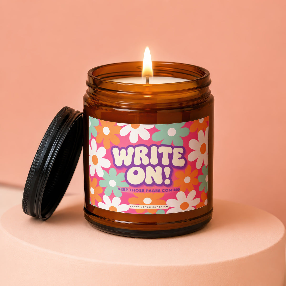 Amber candle with lit wick and floral label saying "WRITE ON! KEEP THOSE PAGES COMING".