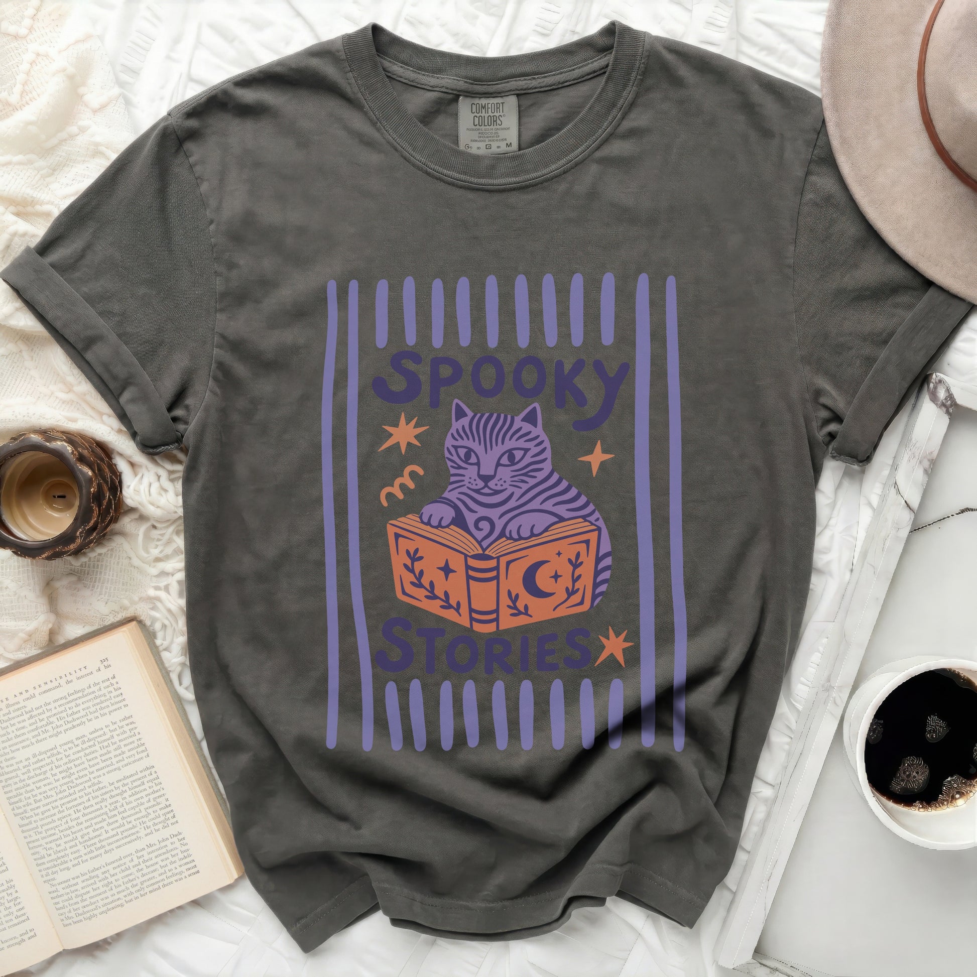 Grey t-shirt with a purple graphic of a cat reading a book and text "SPOOKY STORIES".