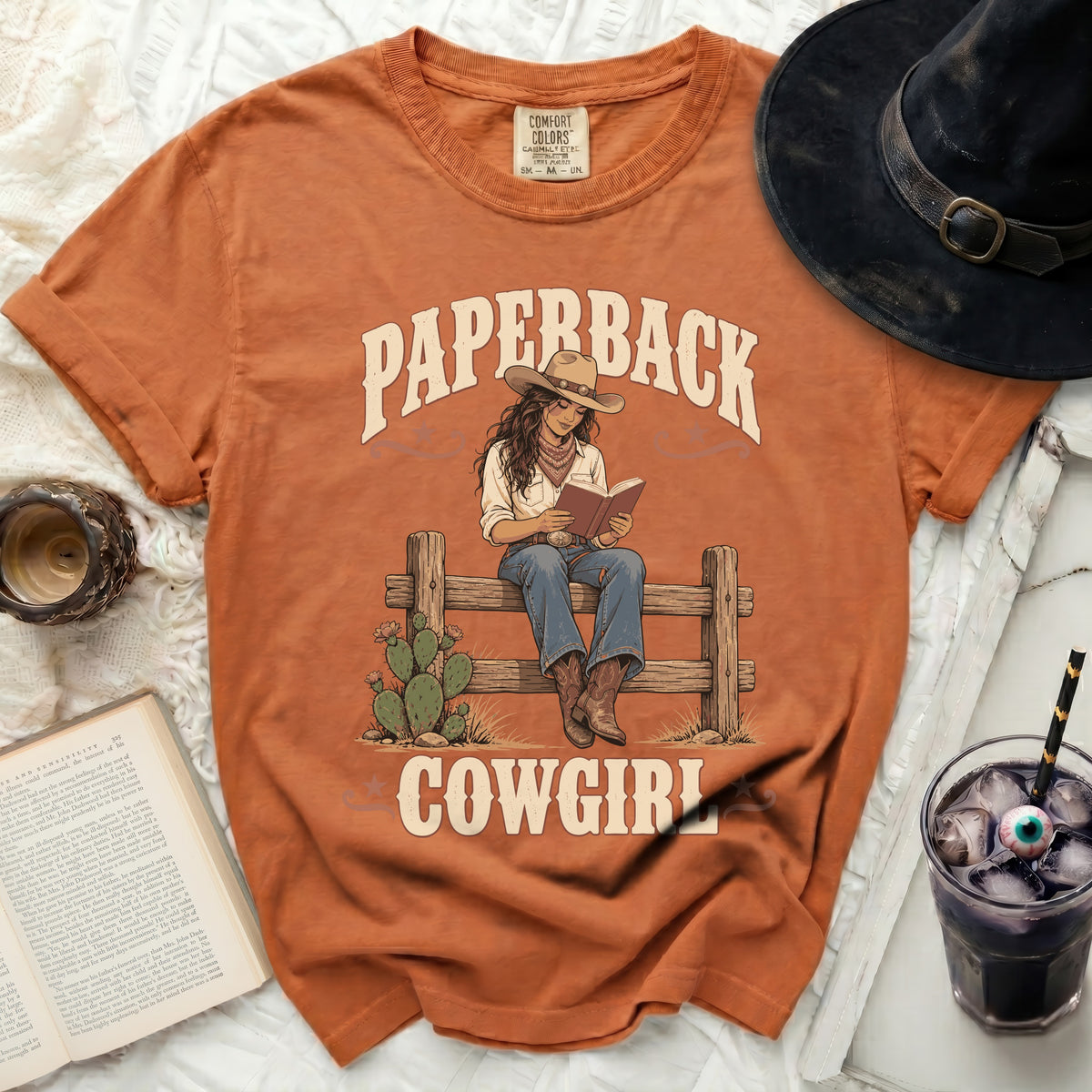 Orange t-shirt graphic: Paperback Cowgirl reading on fence with cactus.