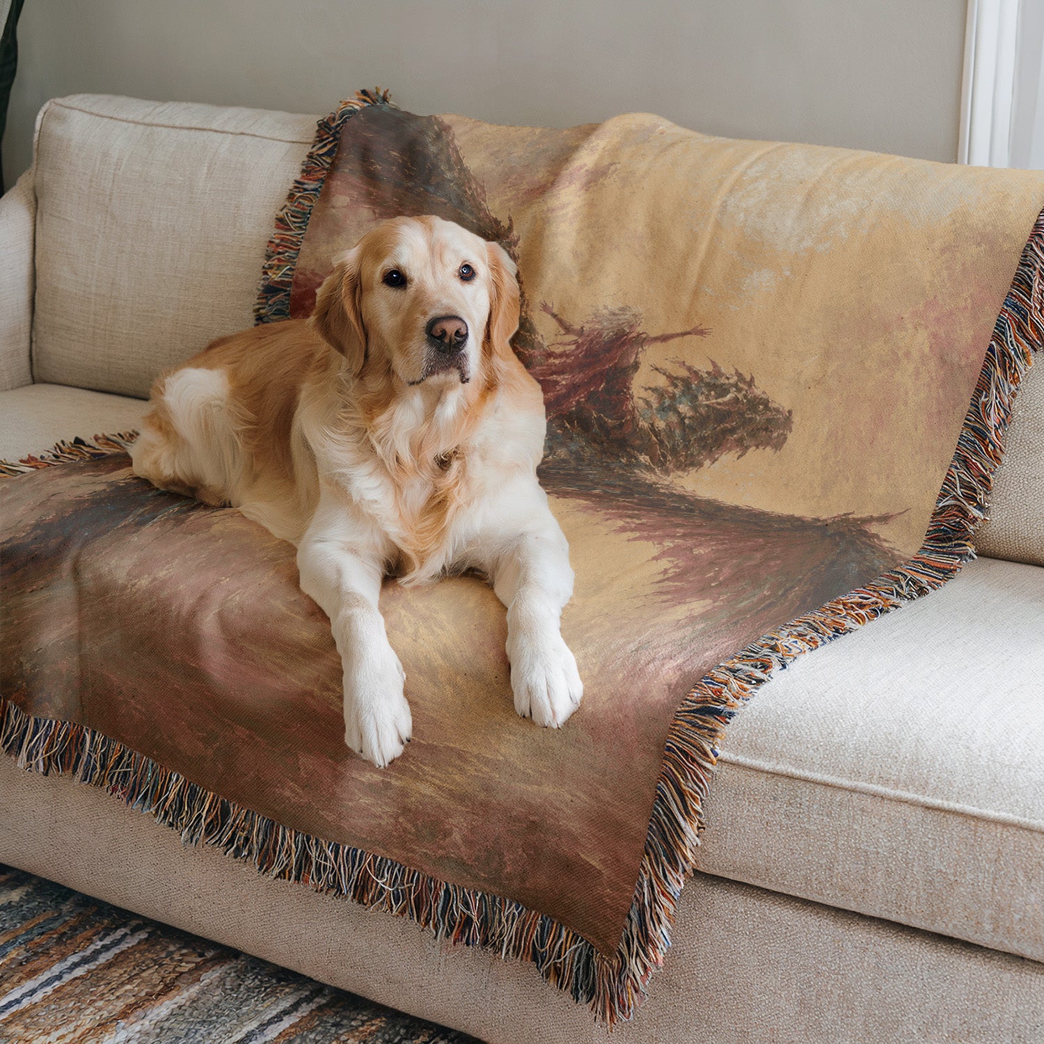 A golden retriever dog is lying on a beige couch, with a colorful blanket featuring a landscape design.