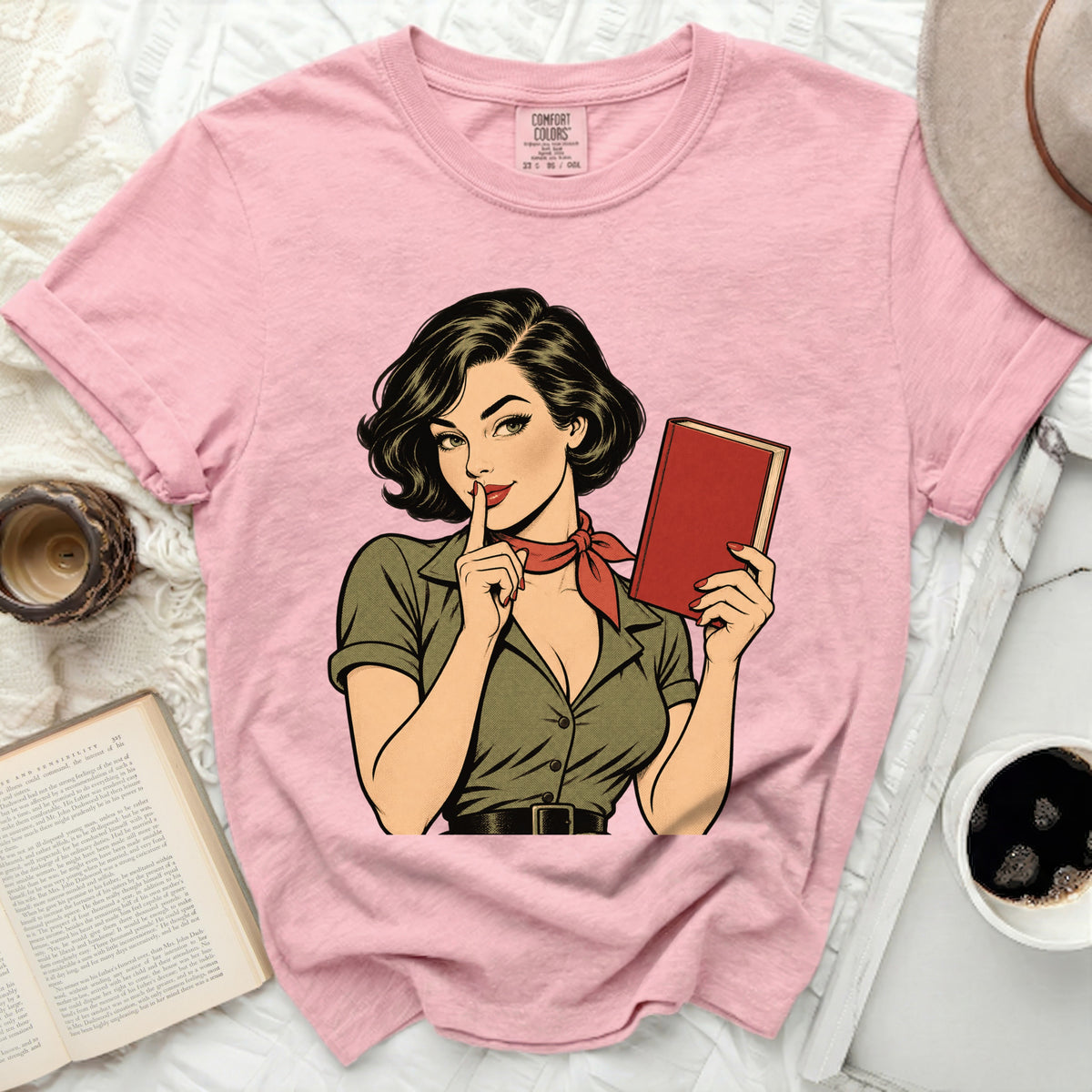 Pink t-shirt with a pop art illustration of a woman holding a book and shushing.