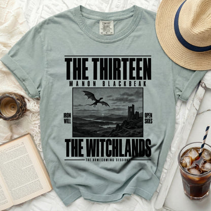 Light blue t-shirt with "The Thirteen Manon Blackbeak The Witchlands" text and dragon artwork.