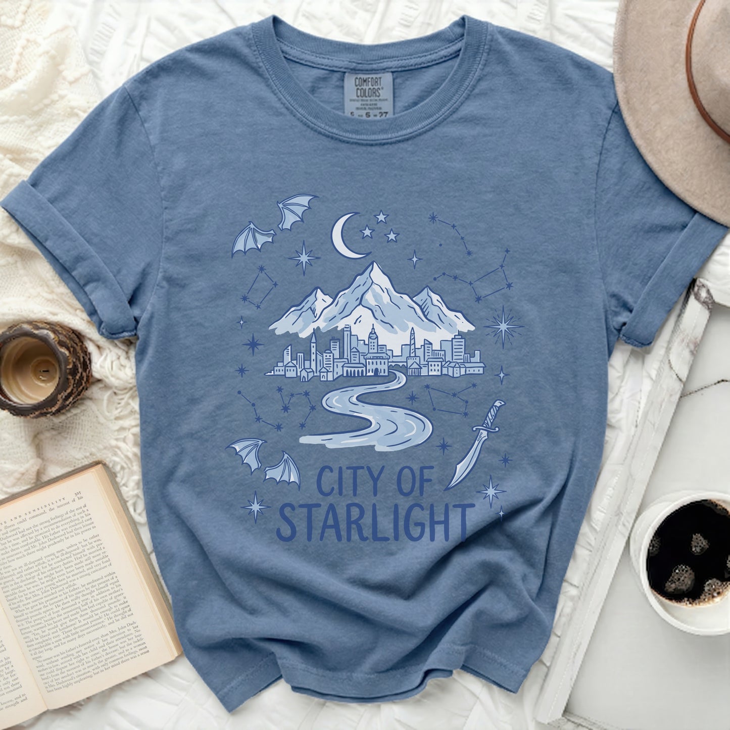 Blue t-shirt with "City of Starlight" graphic showing city, mountains, moon, stars, and bats.