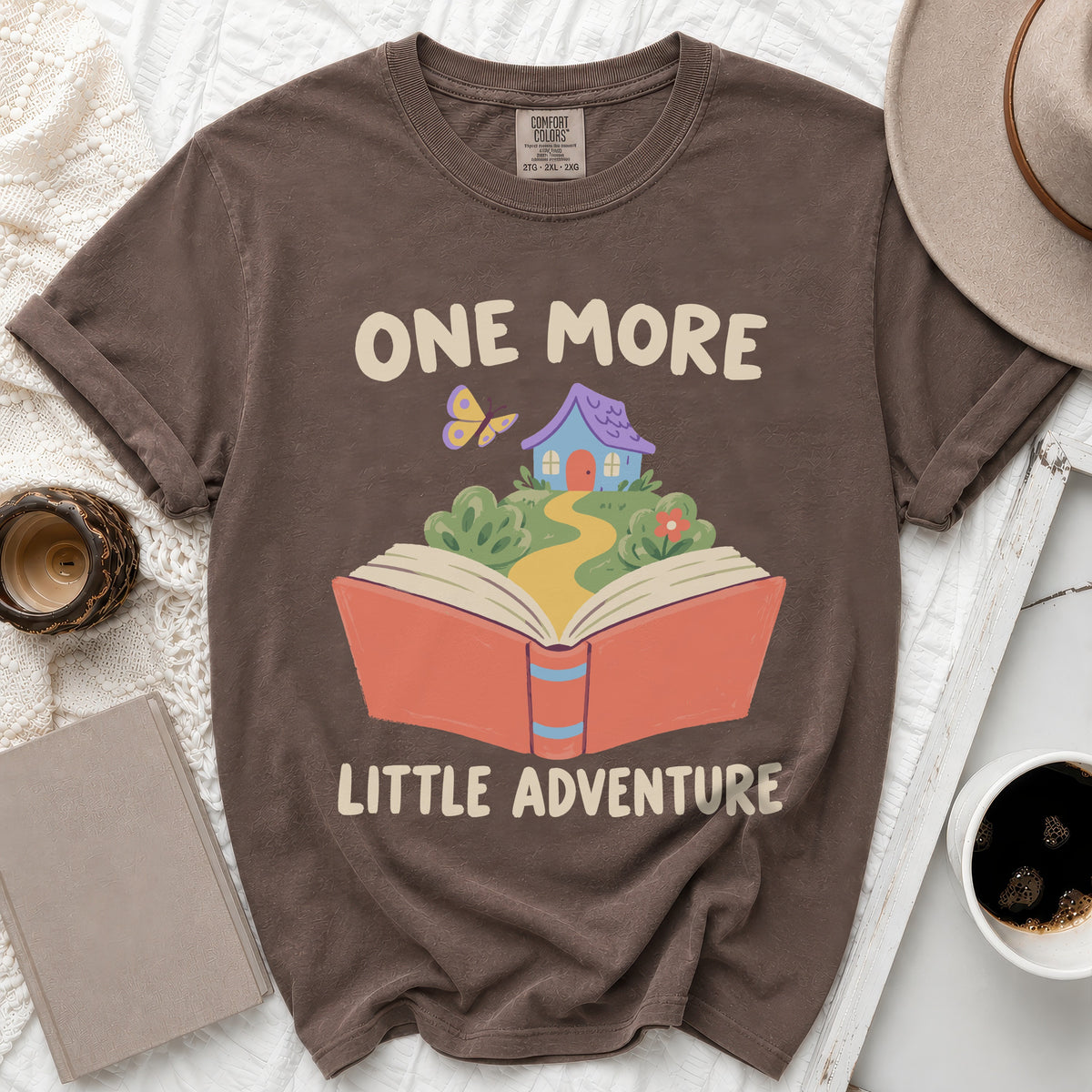 Brown t-shirt with "One More Little Adventure" text and book graphic.