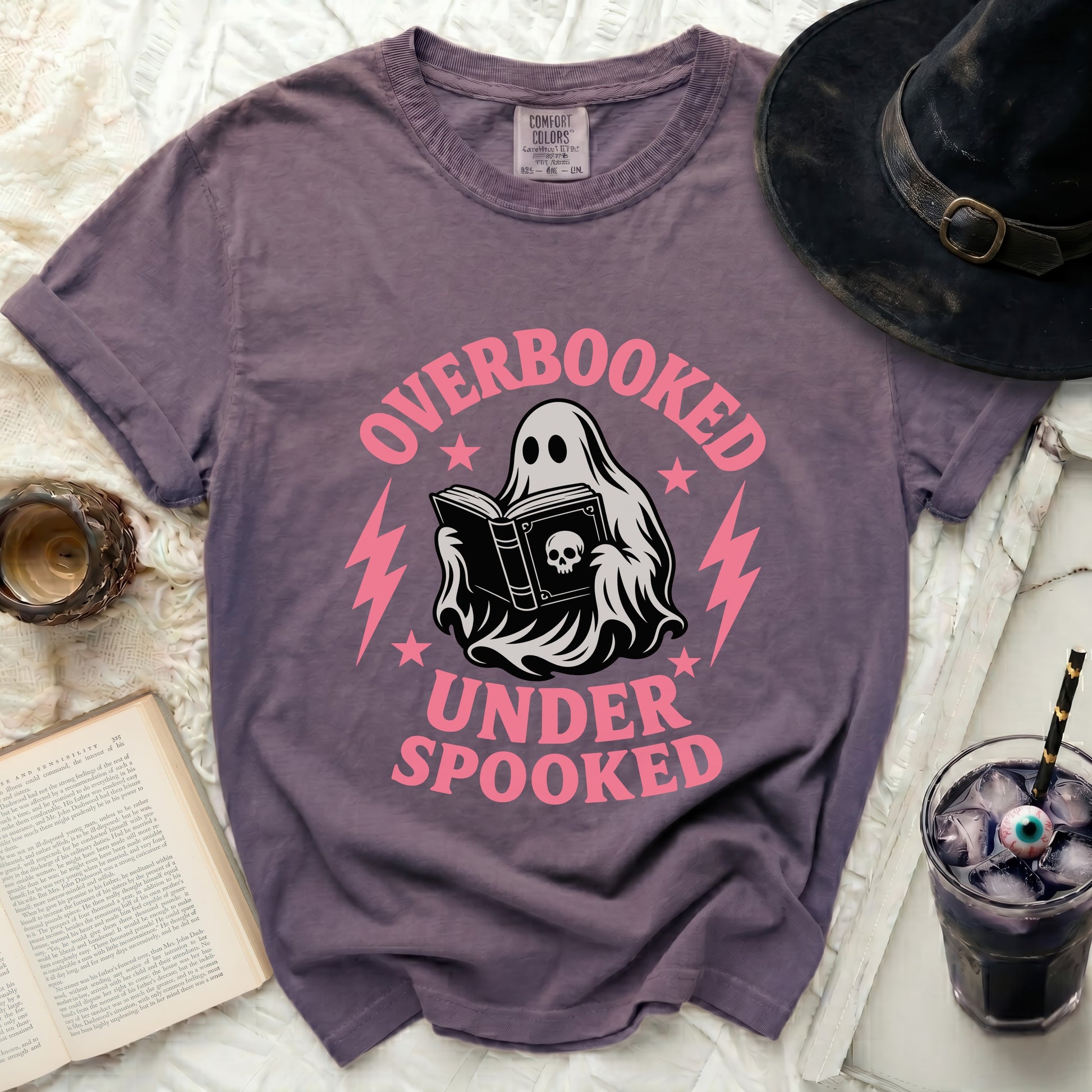 Ghost reading book with "Overbooked Under Spooked" text on purple t-shirt.