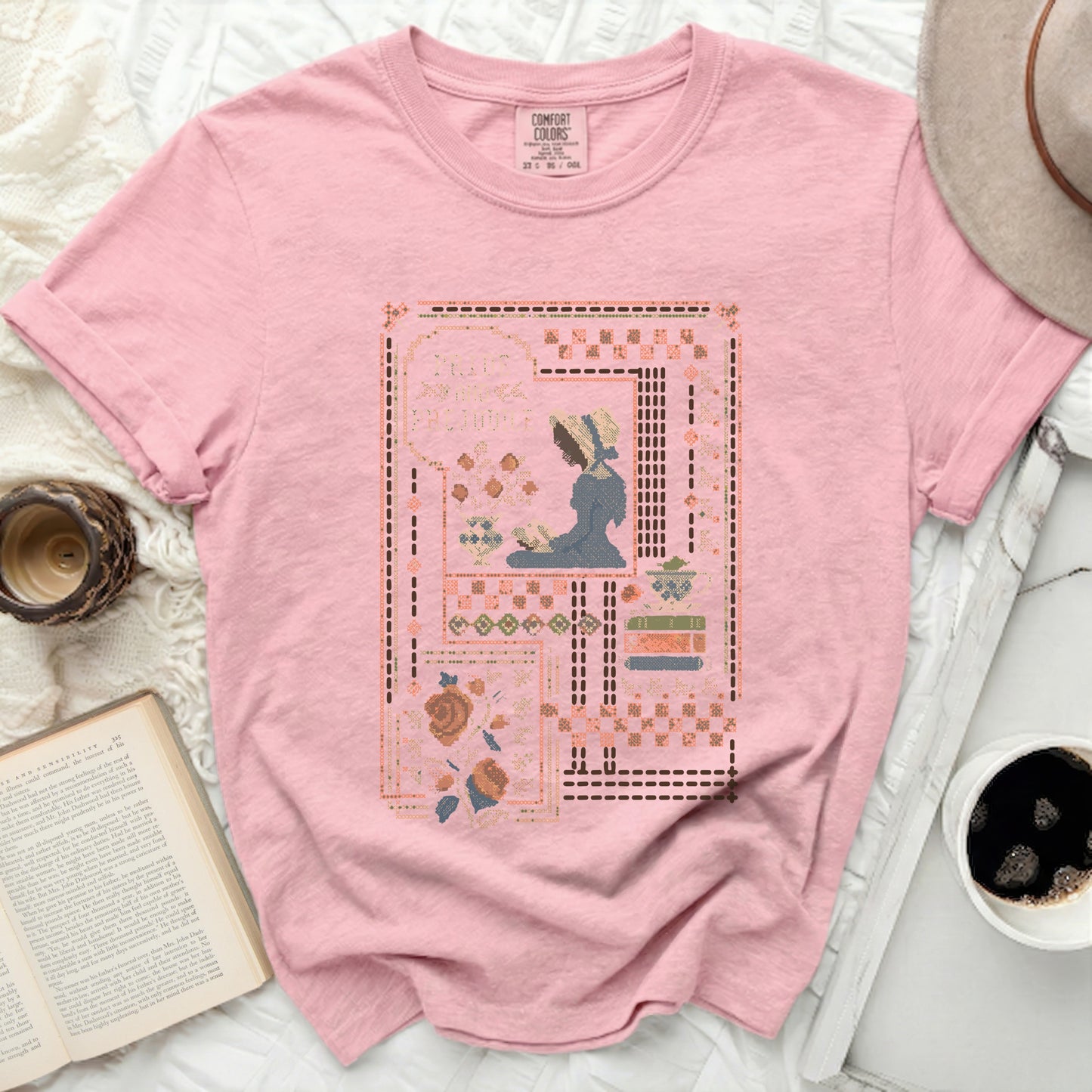 Pink t-shirt with a cross-stitch design of a woman reading.