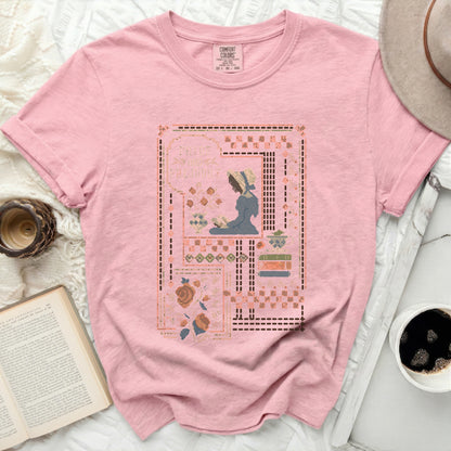 Pink t-shirt with a cross-stitch design of a woman reading.
