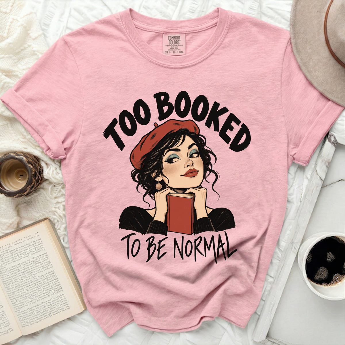 Pink t-shirt with "Too Booked To Be Normal" graphic featuring a woman reading.