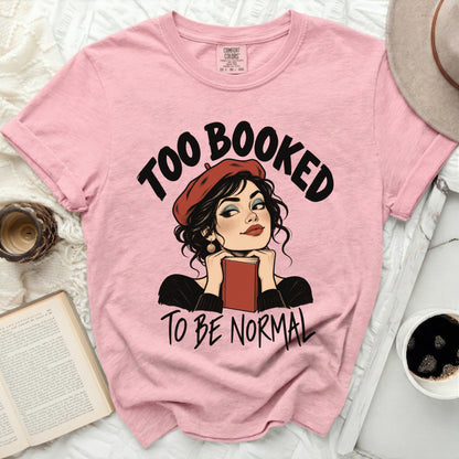 Pink t-shirt with "Too Booked To Be Normal" graphic featuring a woman reading.
