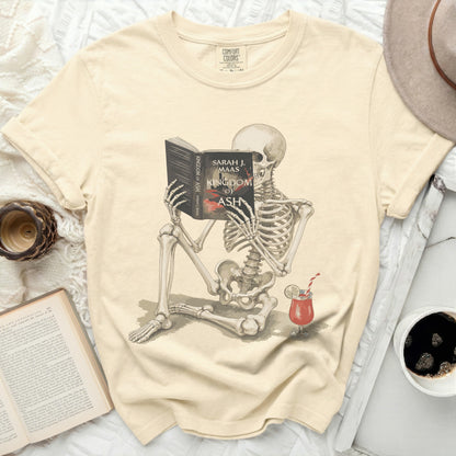 Skeleton reading "Kingdom of Ash" by Sarah J. Maas with a cocktail.