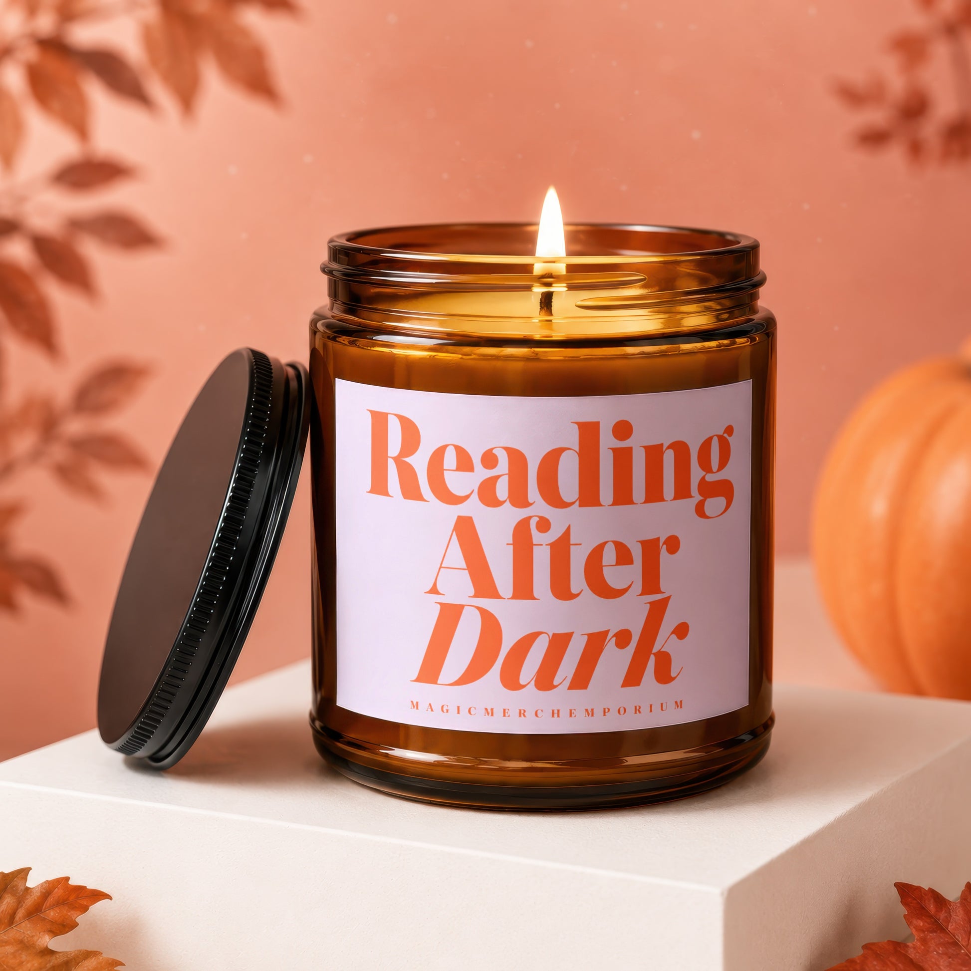 A lit amber glass candle with "Reading After Dark" on the label, beside a pumpkin.
