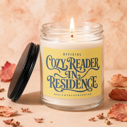 Candle with "Cozy Reader In Residence" text on yellow label.