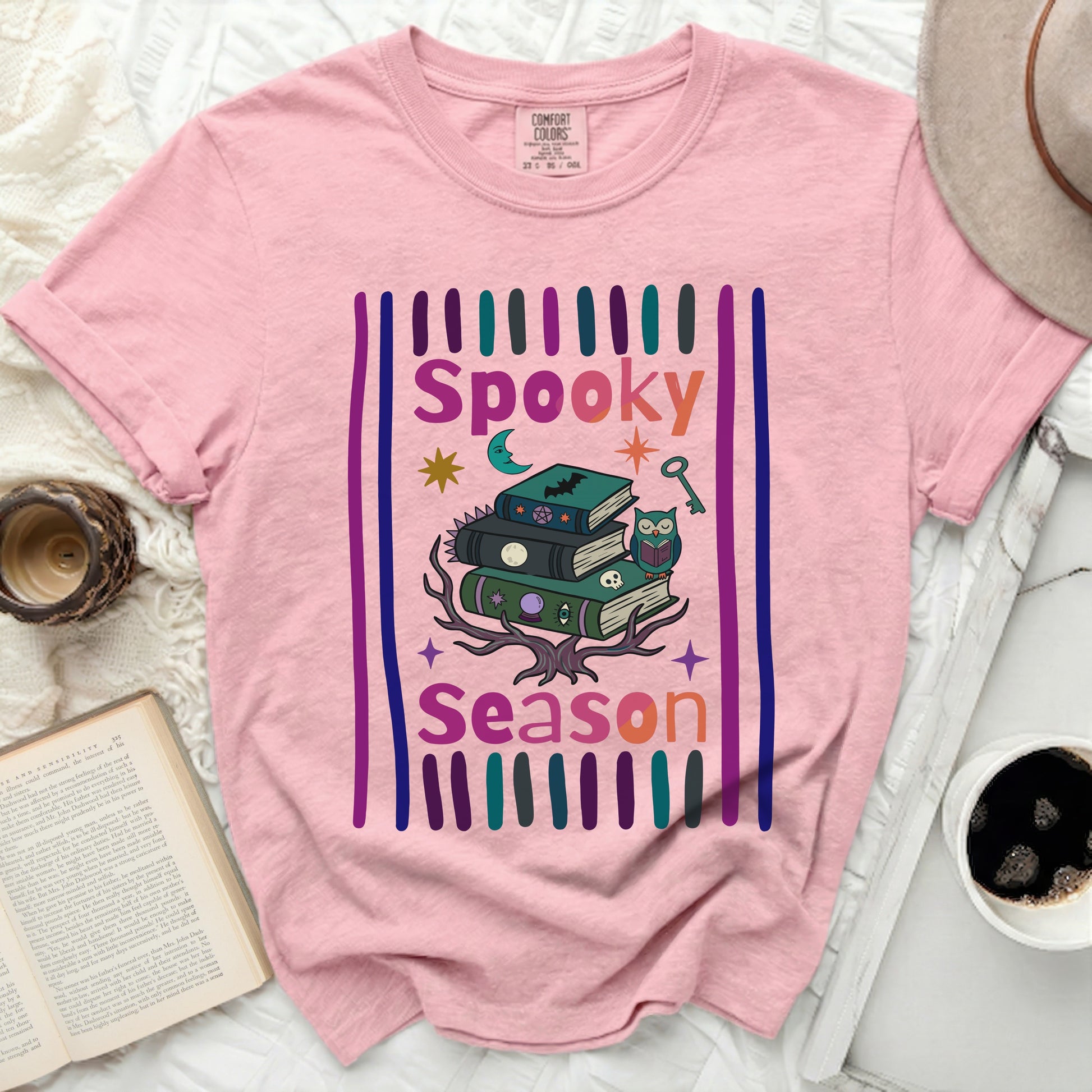 Pink t-shirt with "Spooky Season" gothic graphic and stack of books.