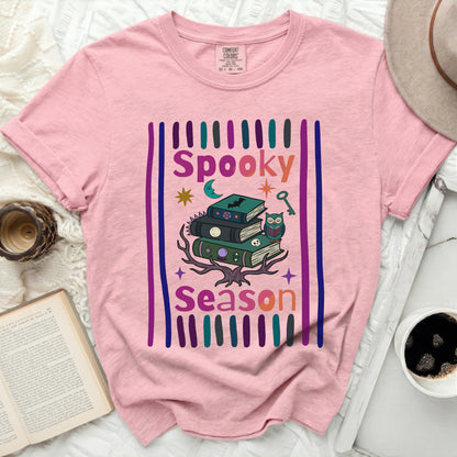 Pink t-shirt with "Spooky Season" gothic graphic and stack of books.