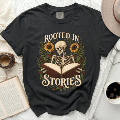 Skeleton reading an open book with sunflowers and foliage, text "ROOTED IN STORIES".