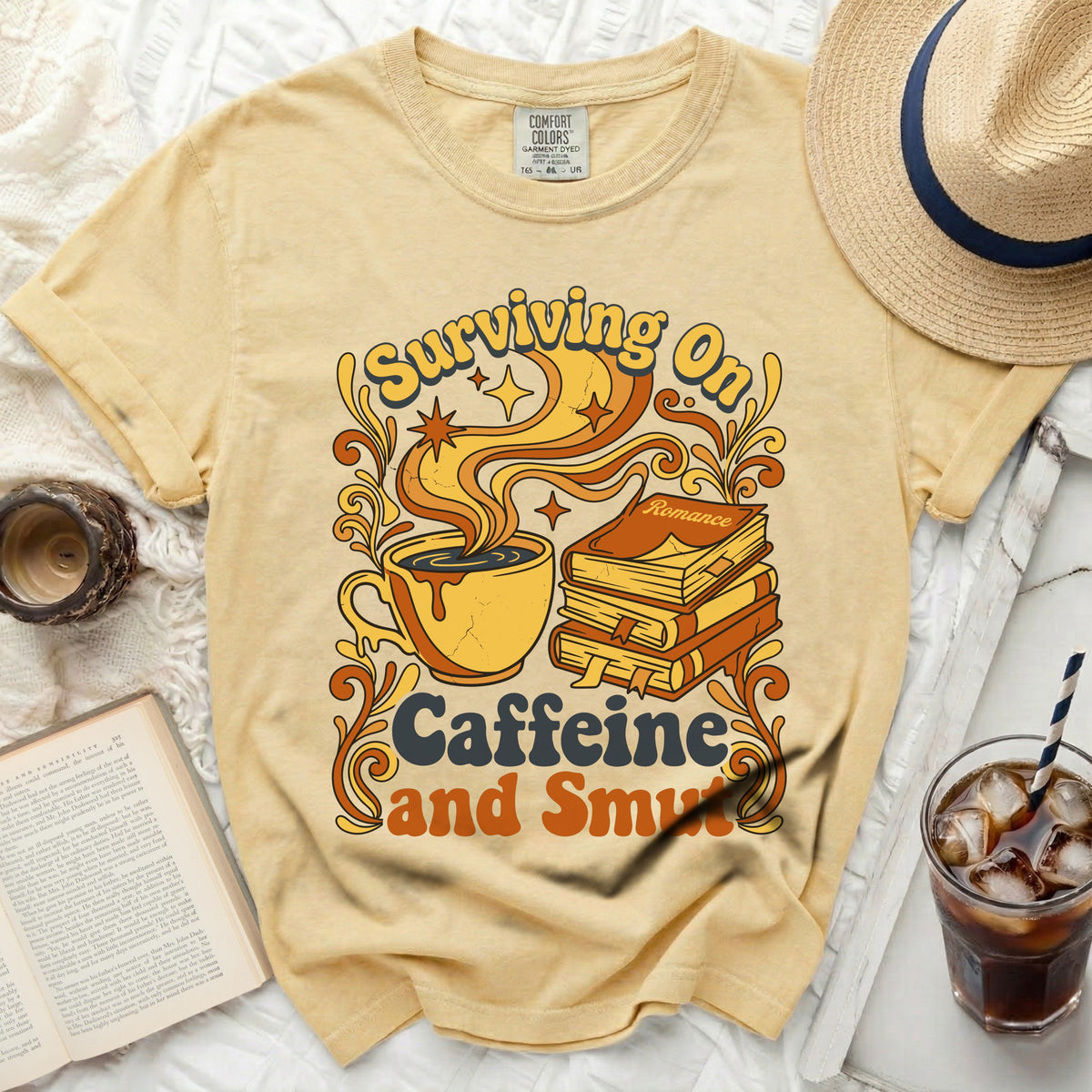 Yellow t-shirt with "Surviving On Caffeine and Smut" graphic and a stack of books.