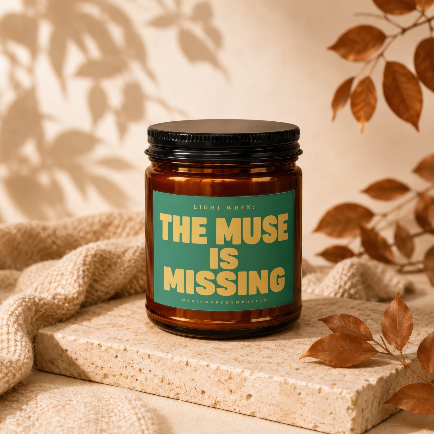 Amber candle with black lid, green label reads "The Muse is Missing".
