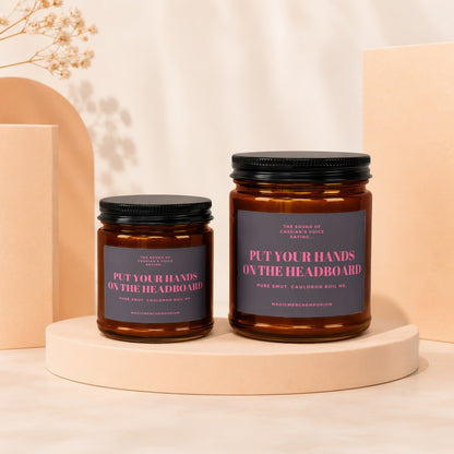 Two amber jar candles with dark labels reading "Put Your Hands On The Headboard" and "Pure Smut. Cauldron Boil Me."