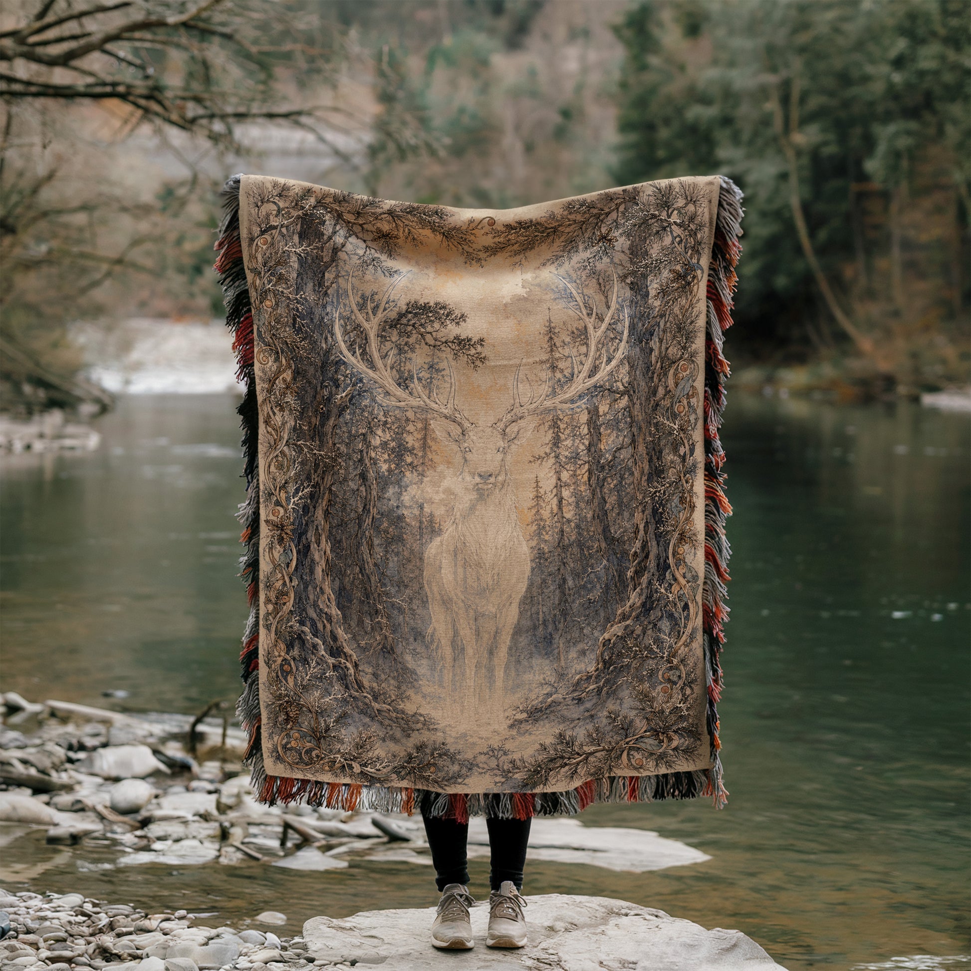 A person stands in front of a river, holding a large rug with a deer design on it.