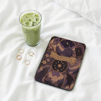 Book with enchanting mystical art, featuring a wolf, castle, and text, next to iced matcha and rings.
