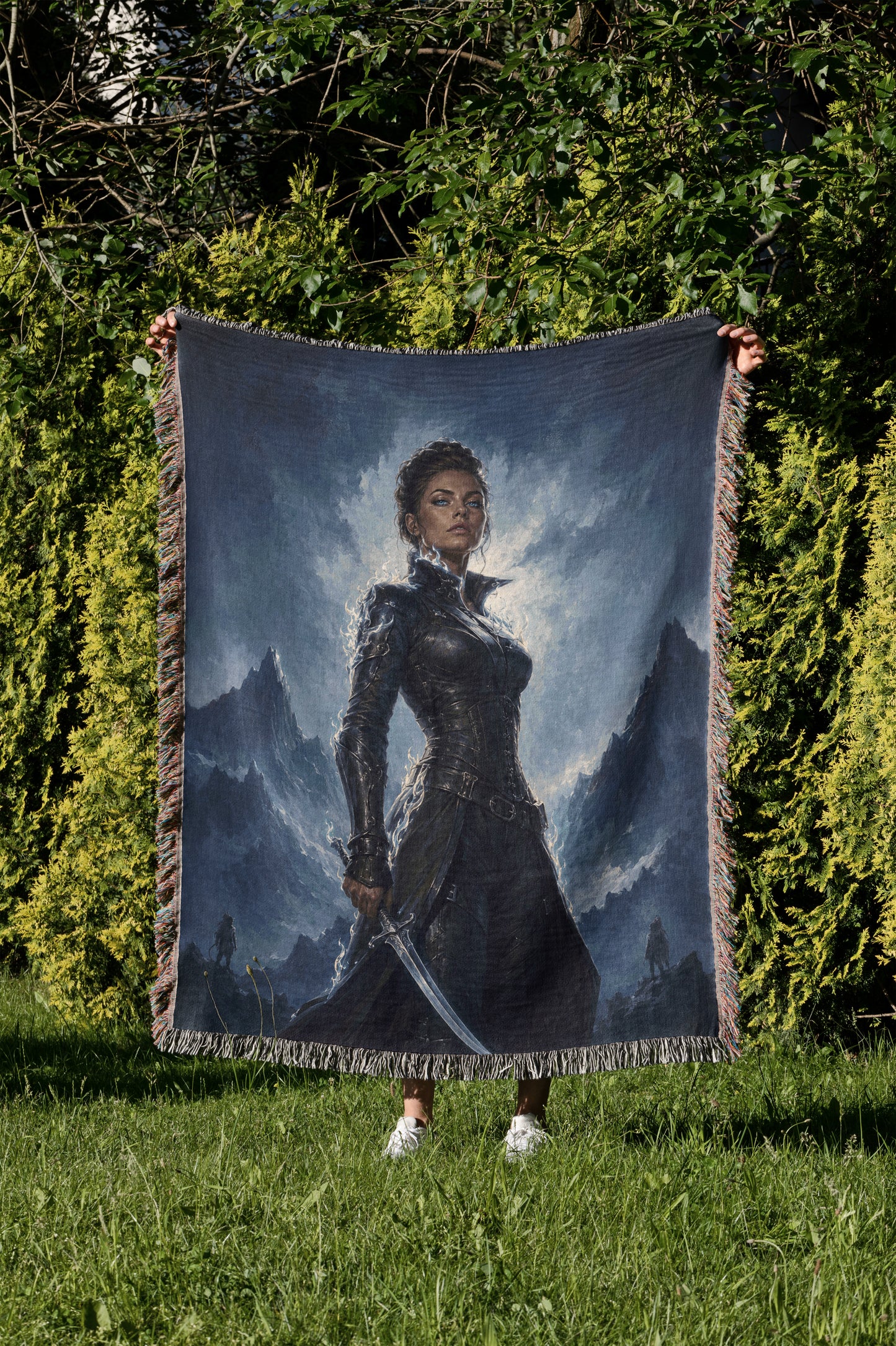 A person is holding up a large tapestry or blanket featuring a painting of a woman in a dark outfit, standing in a grassy field with mountains in the background.