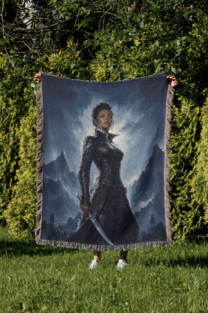 A person is holding up a large tapestry or blanket featuring a painting of a woman in a dark outfit, standing in a grassy field with mountains in the background.