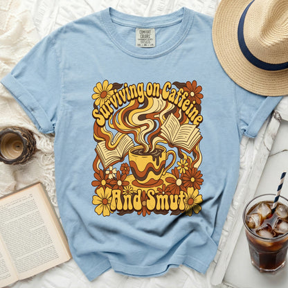 Light blue t-shirt with graphic design of coffee cup, books, and flowers.