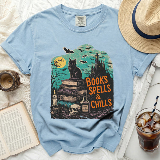 Light blue t-shirt with Halloween graphic: black cat, books, skull, castle, bats, moon.