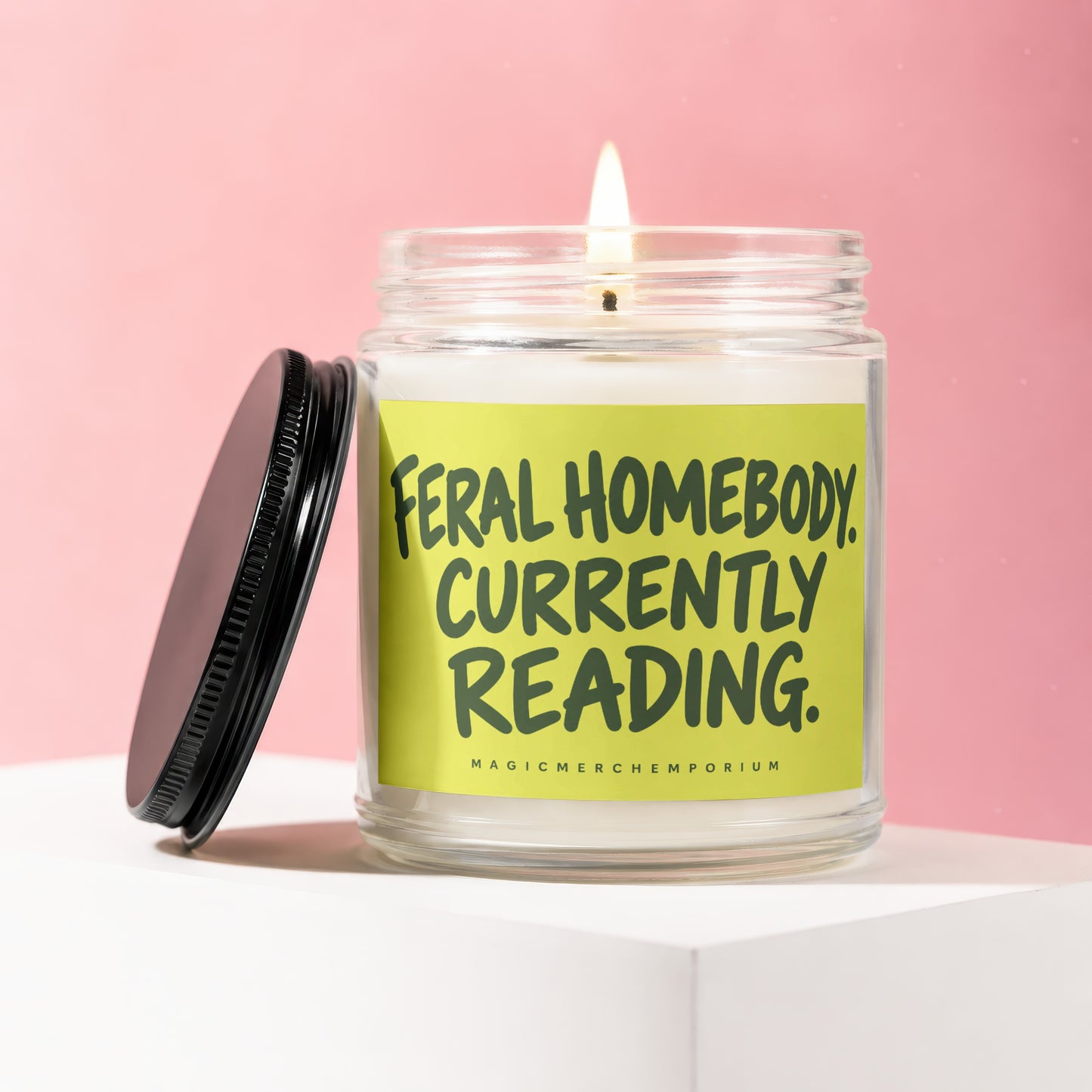 Glass candle with lit wick and "Feral Homebody Currently Reading." text on a lime green label.