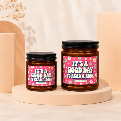 Two amber glass candles with pink floral labels reading "It's a good day to read a book".