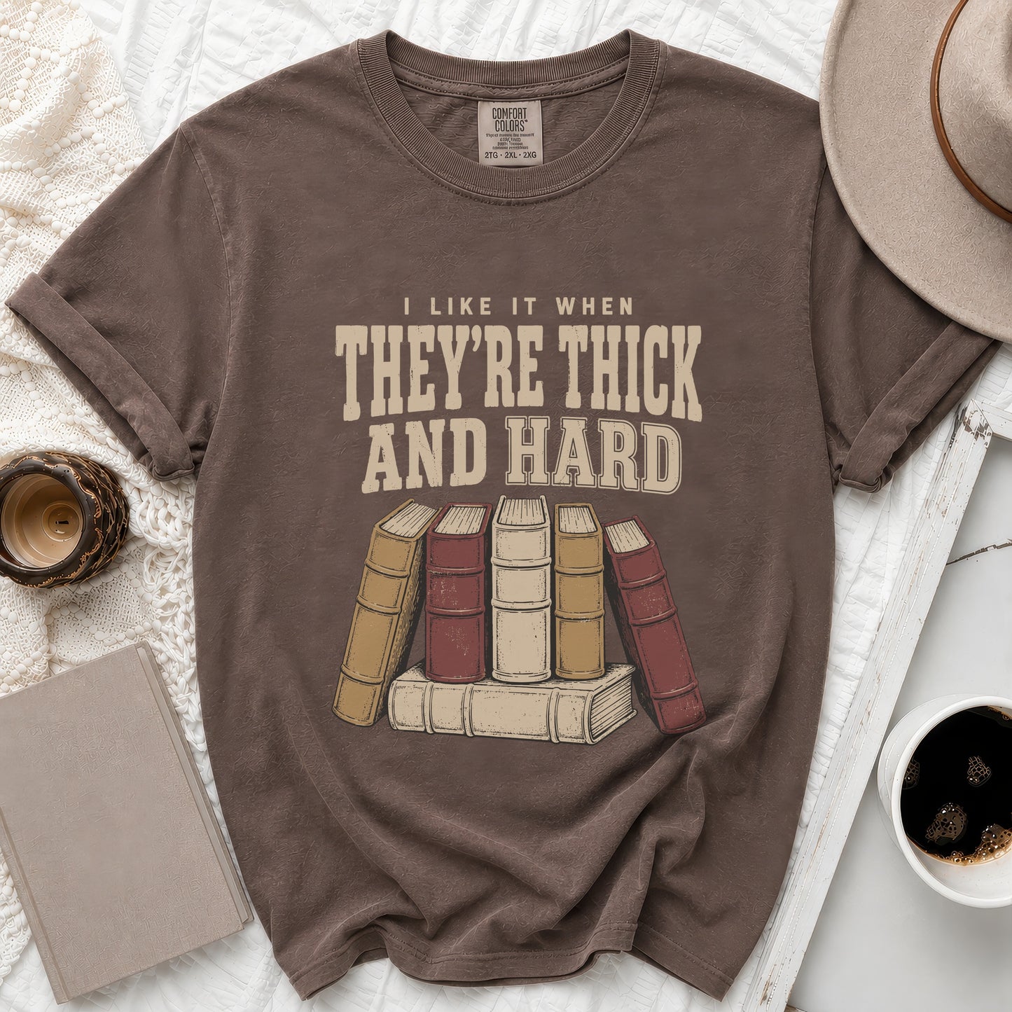 Brown t-shirt with text "I LIKE IT WHEN THEY'RE THICK AND HARD" and vintage book graphic.