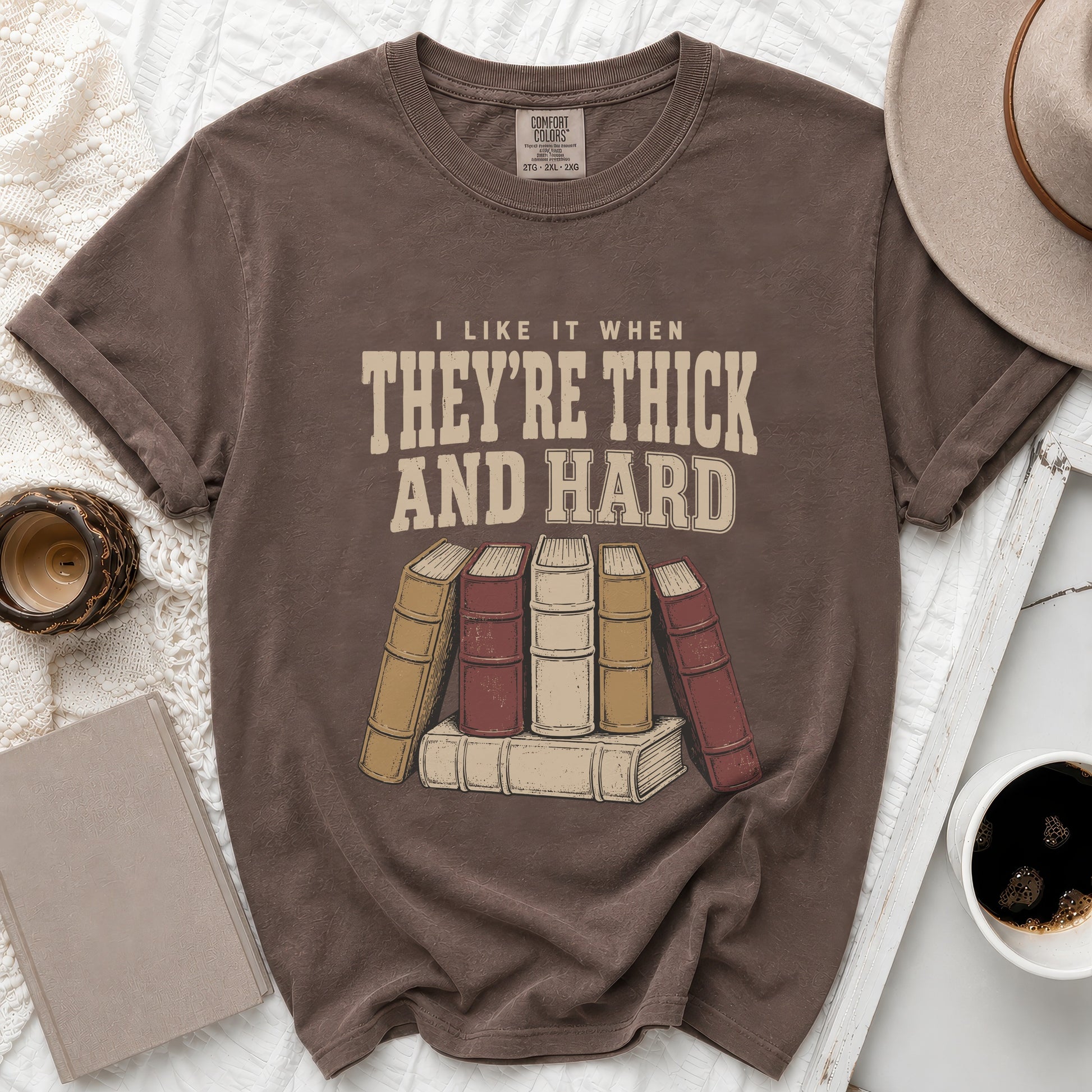 Brown t-shirt with text "I LIKE IT WHEN THEY'RE THICK AND HARD" and vintage book graphic.