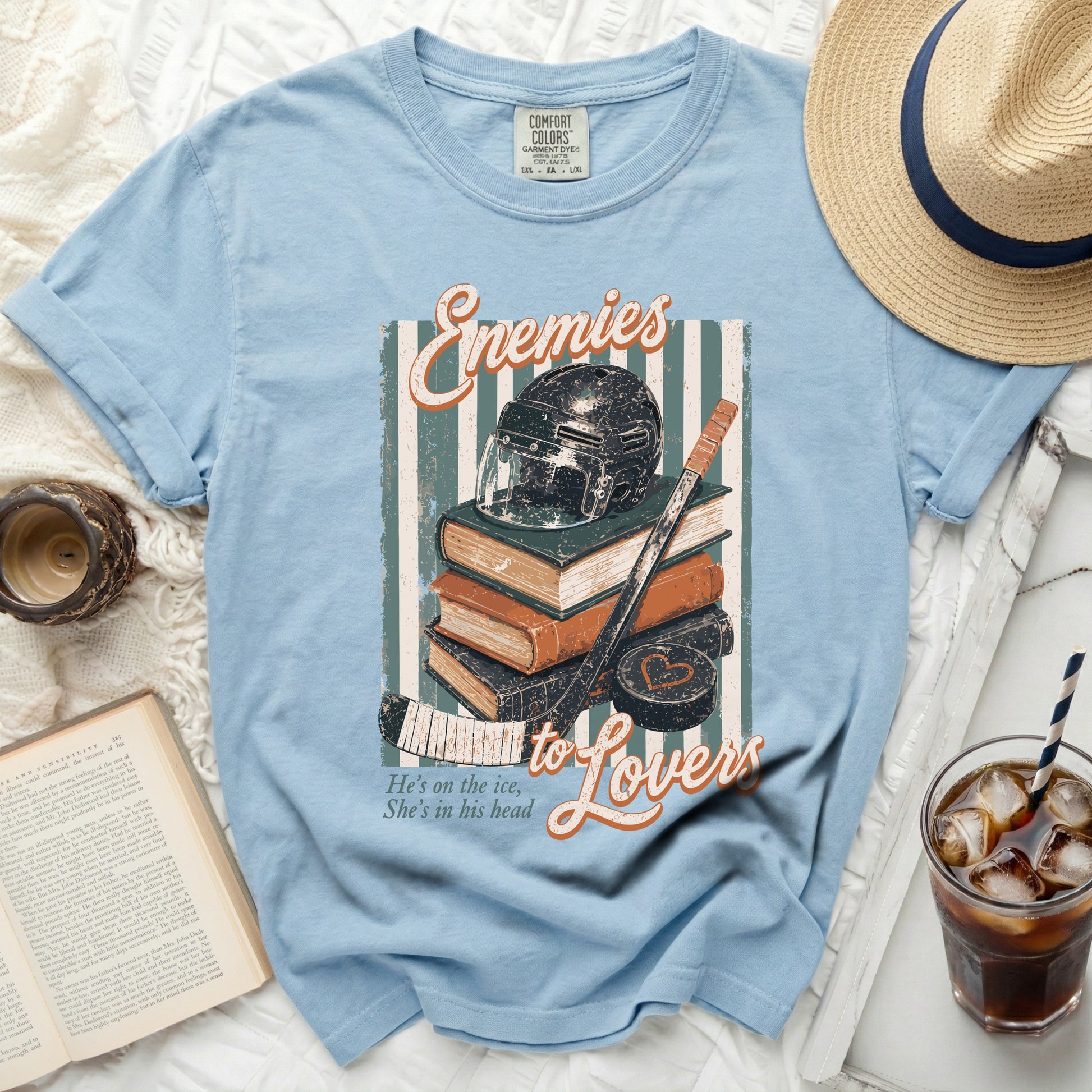 Light blue t-shirt with "Enemies to Lovers" graphic featuring hockey gear and books.