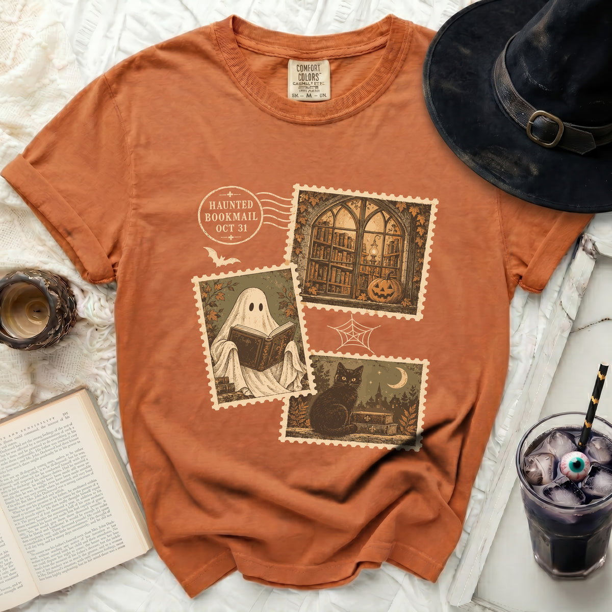 Orange t-shirt with vintage stamps featuring a ghost reading, a black cat, and a library window.