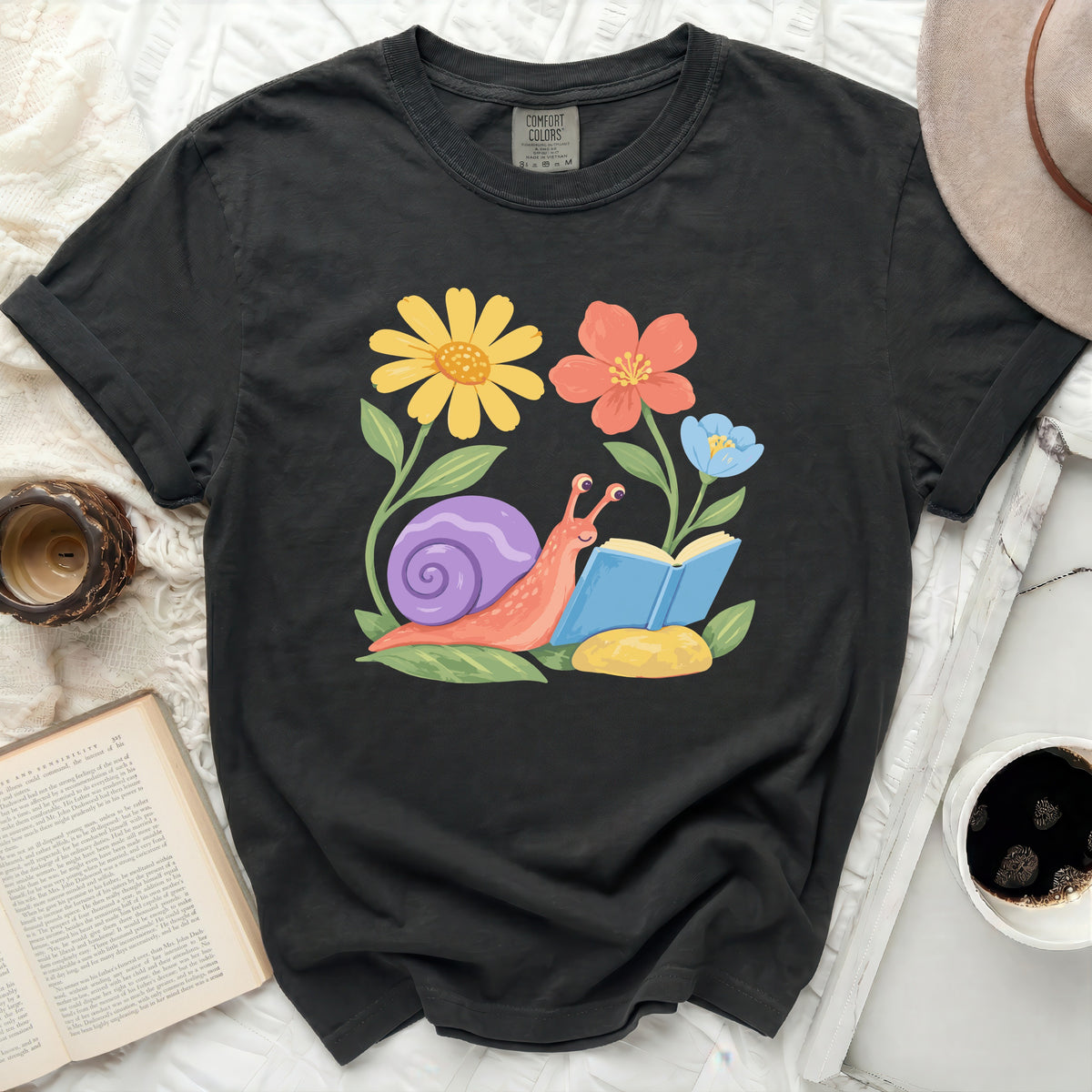 Graphic tee with a snail reading a book surrounded by colorful flowers.