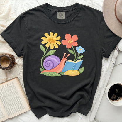 Graphic tee with a snail reading a book surrounded by colorful flowers.
