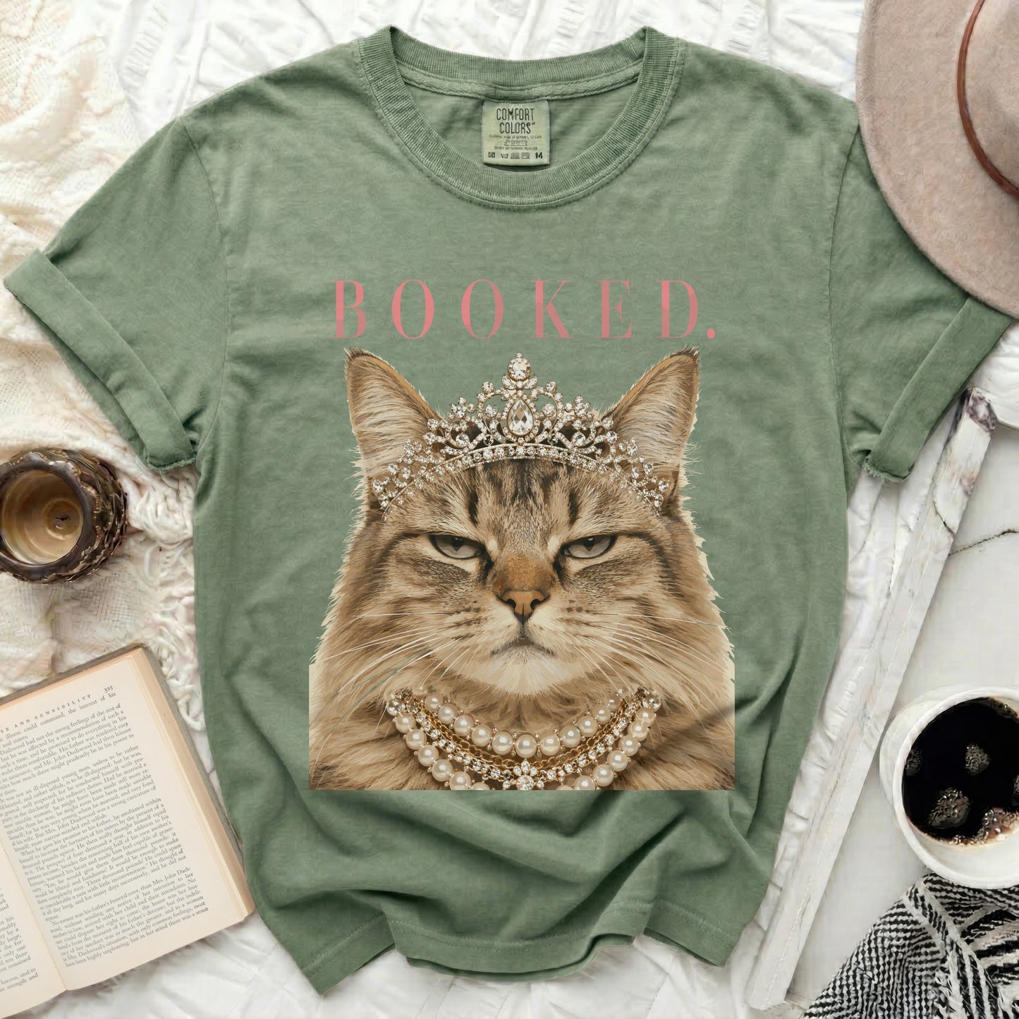 Green t-shirt with a cat wearing a tiara and pearls, text "BOOKED."