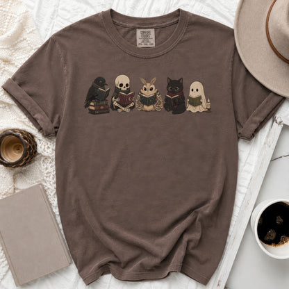 Brown comfort colors shirt with graphic of crow, skeleton, moth, cat, and ghost reading books.