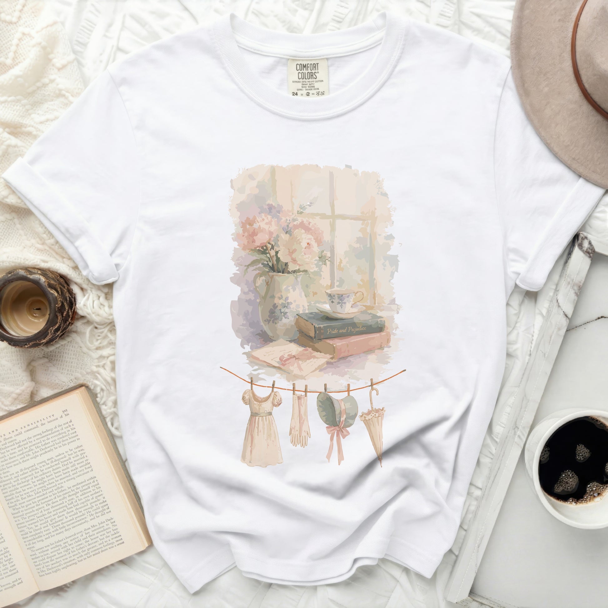 White t-shirt with watercolor print of clothes on a line, books, and flowers.