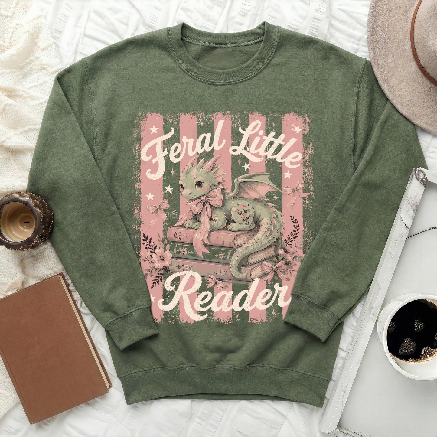 Green sweatshirt with a cute dragon on books, reading "Feral Little Reader."